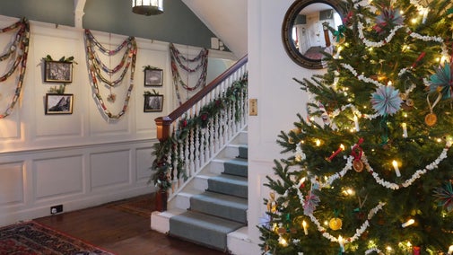 A decorated Christmas tree stands on the far right-hand side of the screen, with a decorated staircase and walls in the background